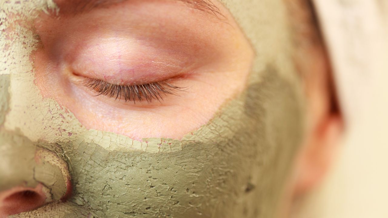 close-up de um rosto, na área do olho, com máscara de argila verde para cuidados da pele pós-sol